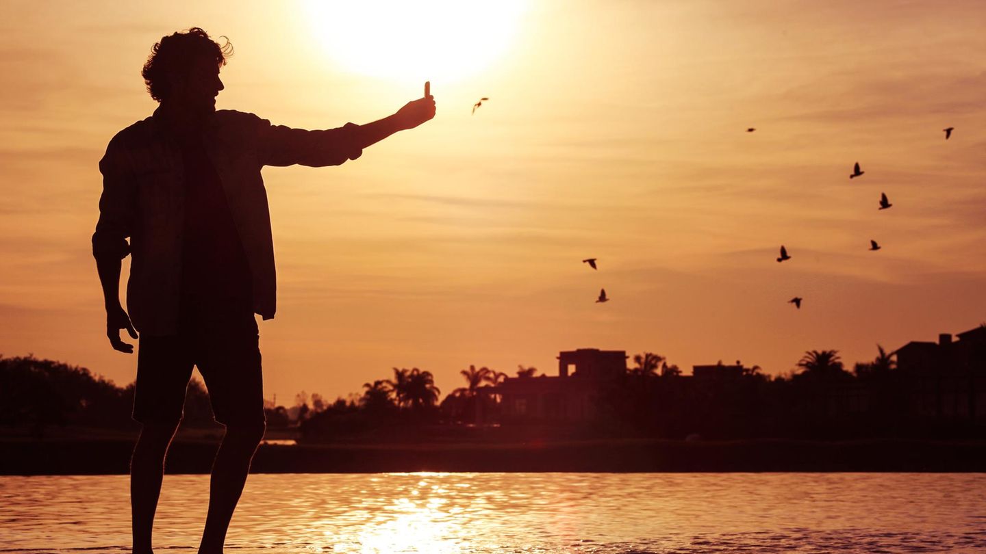 Ein junger Mann steht im Sonnenuntergang am Wasser