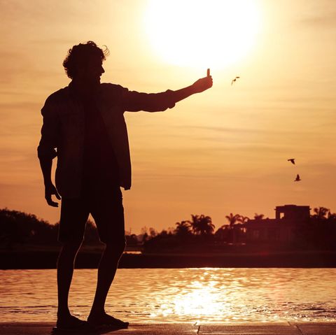 Ein junger Mann steht im Sonnenuntergang am Wasser