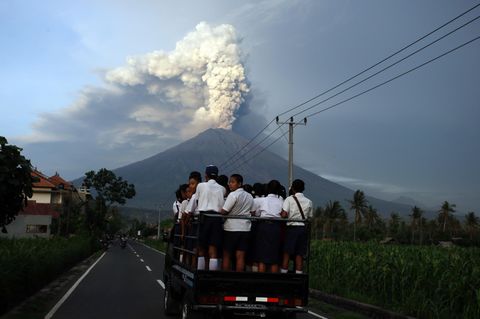 Ein Kleintransporter auf Bali fährt mit Schülern auf der Ladefläche auf den Vulkan Gunung Agung zu, der Rauch und Asche speiht