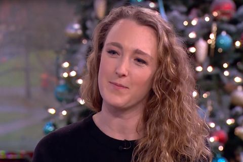 Eine junge Frau mit blonden Locken und einem schwarzen Rundkragen-Pulli sitzt in einem weihnachtlich dekorierten TV-Studio