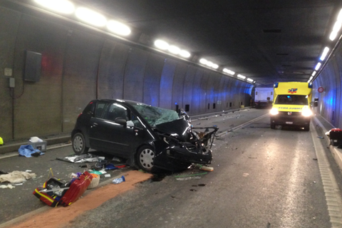 Ein schwarzer Kleinwagen steht quer im Gotthard-Tunnel. Die Front ist komplett zerstört. Im Hintergrund steht ein Krankenwagen.