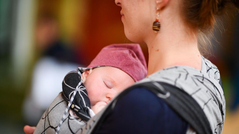 Eine junge Mutter trägt ihr Baby auf der Brust Eine junge Mutter trägt ihr Baby auf der Brust