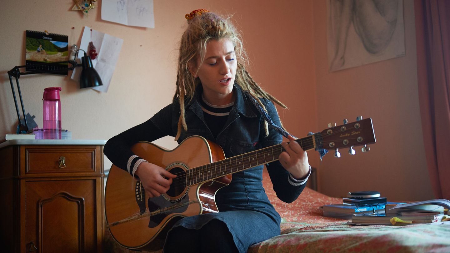 Natia Todua auf sitzt mit einer Gitarre auf dem Bett.