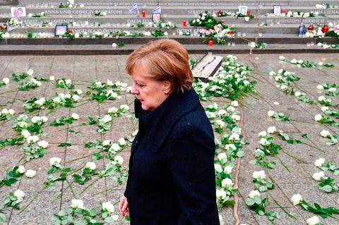 Im dunklen Mantel geht Angela Merkel über den Breitscheidplatz, auf dem weiße Rosen für die Opfer des Terroranschlag liegen