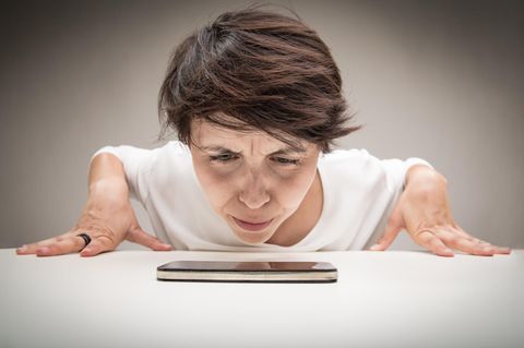 Eine Frau schaut skeptisch ihr iPhone an. Ist es langsamer geworden oder gar gedrosselt?