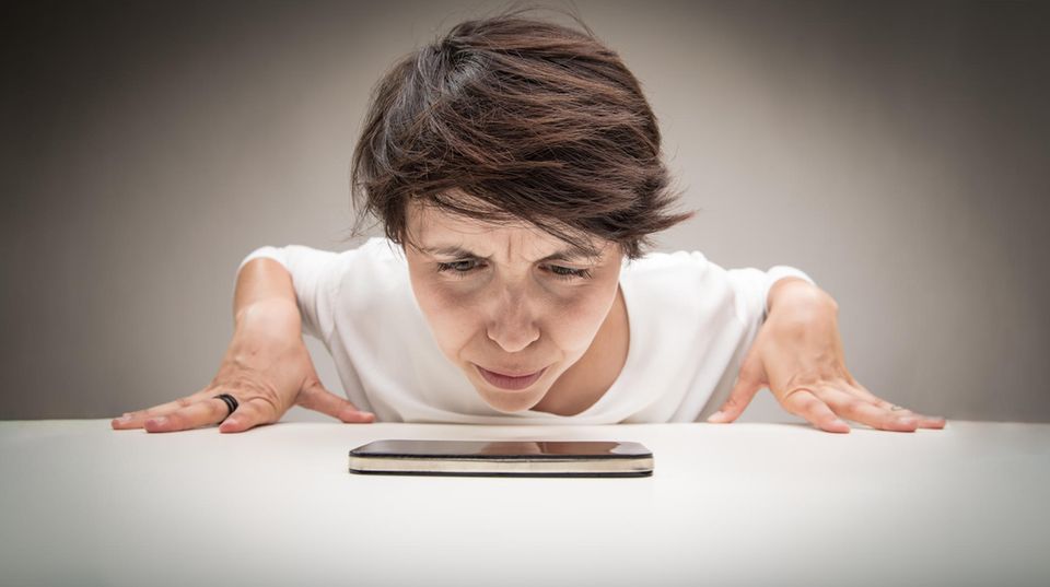 Eine Frau schaut skeptisch ihr iPhone an. Ist es langsamer geworden oder gar gedrosselt?