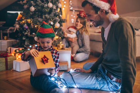 Eine Familie sitzt vorm Weihnachtsbaum und öffnet ihre Geschenke