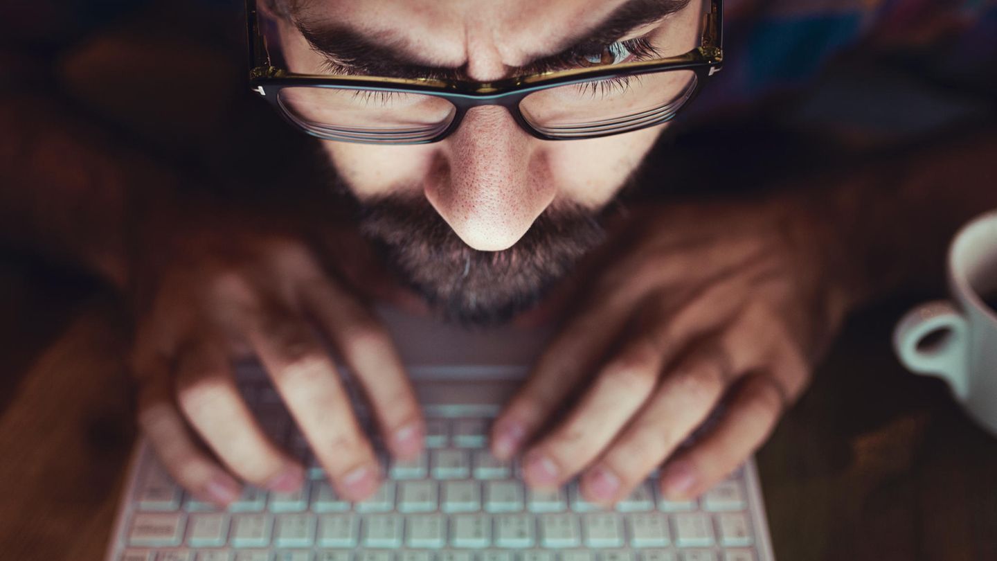 Ein Mann mit Bart gibt am Laptop sein Passwort ein und schaut dabei irritiert