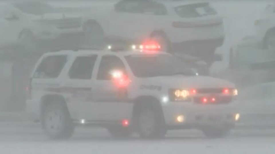 Im Schneetreiben fährt ein SUV der Polizei mit Blaulicht auf einer Autobahn. Auf der Gegenfahrbahn steht ein Autotransporter.