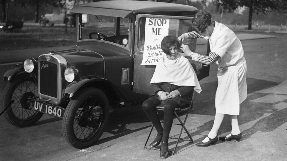 Ein altes Foto: Es zeigt eine Frau, die sich auf der Straße von einer Friseurin die Haare schneiden lässt