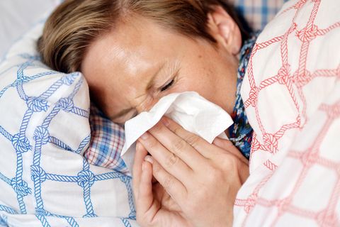 Grippewelle 2017/2018: Eine Frau liegt mit einer Grippe-Erkrankung im Bett und schnäuzt in ein Taschentuch