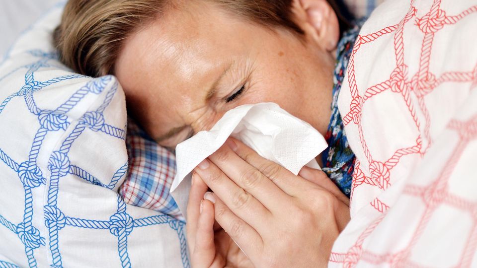 Grippewelle 2017/2018: Eine Frau liegt mit einer Grippe-Erkrankung im Bett und schnäuzt in ein Taschentuch