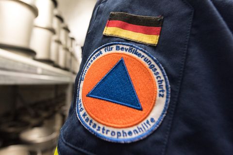 Auf dem Ärmel einer dunkelblauen Uniform ist eine aufgenähte Deutschlandflagge und darunter das Logo des Bundesamtes zu sehen