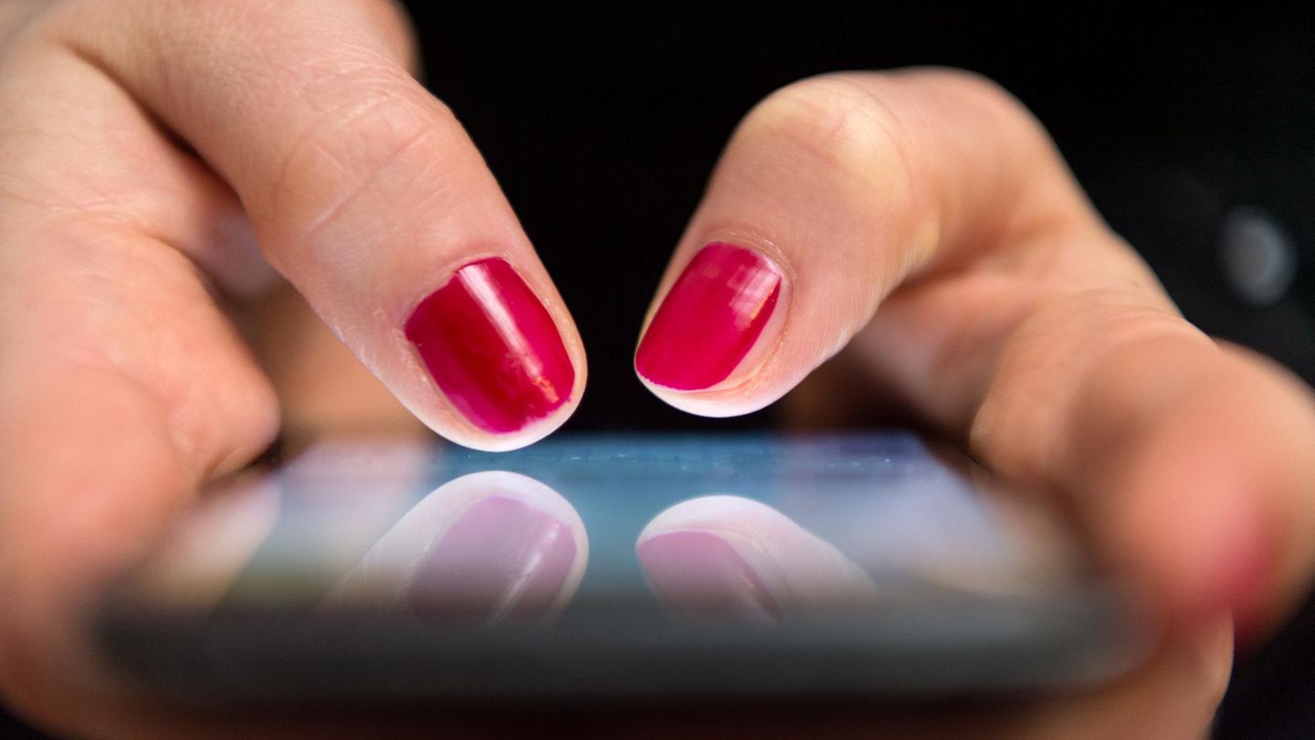 Zwei lackierte Fingernägel tippen auf einem Smartphone