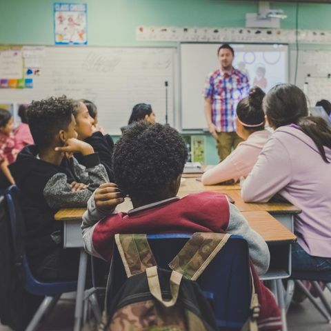 Kinder sitzen in der Schule im Unterricht und gucken nach vorne zum Lehrer.
