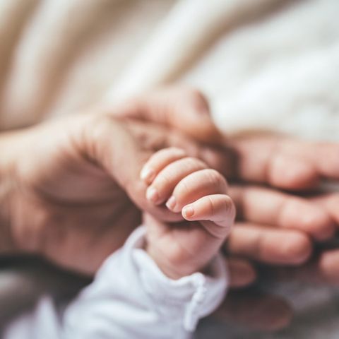 Baby hält sich am Daumen seiner Mutter fest