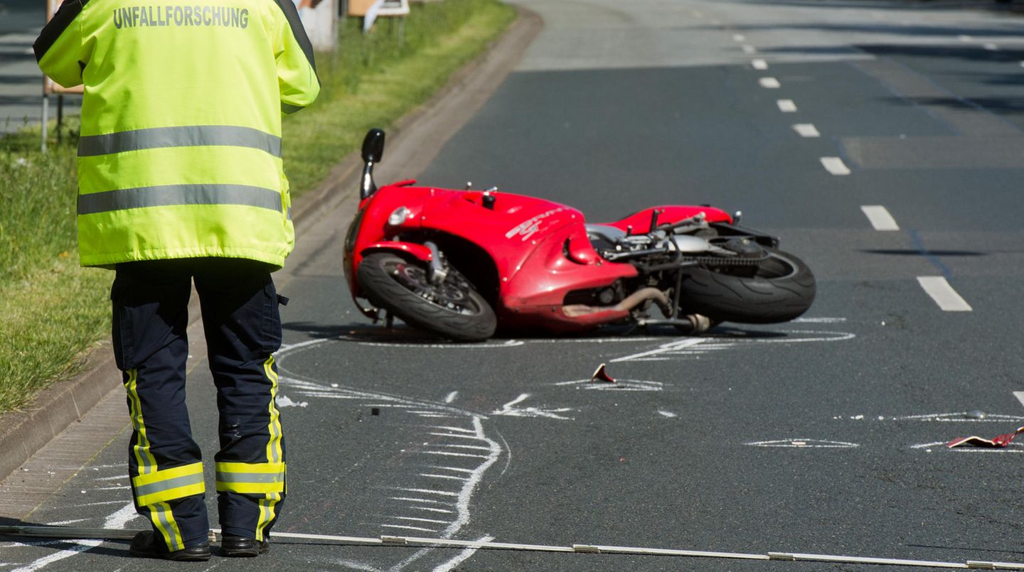 Ein Polizist in neongelber Jacke mit "Unfallforschung" auf dem Rücken steht vor einem kaputten Motorrad auf einer Straße