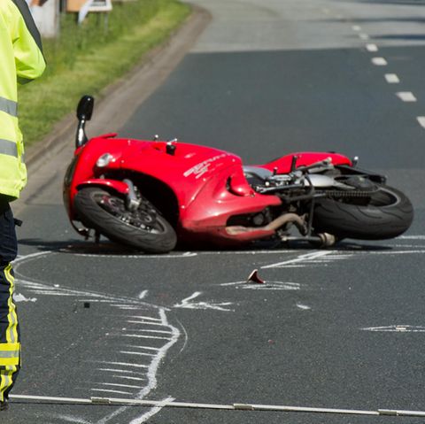 Ein Polizist in neongelber Jacke mit "Unfallforschung" auf dem Rücken steht vor einem kaputten Motorrad auf einer Straße