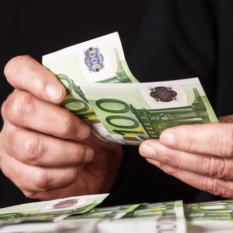 Hände mit 100-Euro-Geldscheinen, die gezählt und auf einem Tisch abgelegt werden.