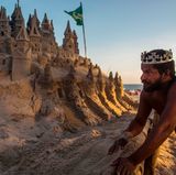 Der Brasilianer Marcio Mizael Matolias steht vor seiner Sandburg in Rio und trägt eine Krone.