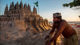 Der Brasilianer Marcio Mizael Matolias steht vor seiner Sandburg in Rio und trägt eine Krone.