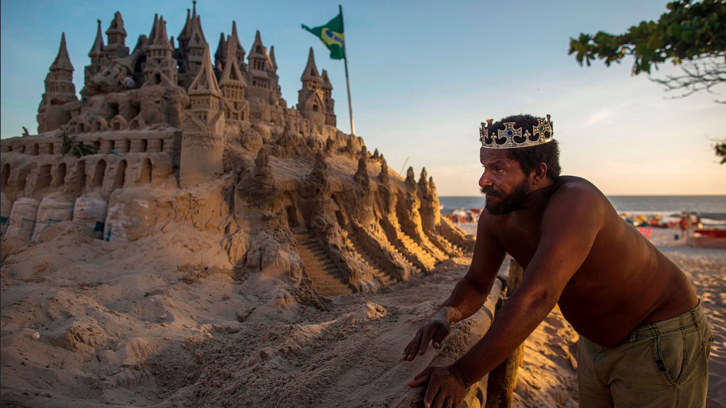 Der Brasilianer Marcio Mizael Matolias steht vor seiner Sandburg in Rio und trägt eine Krone.