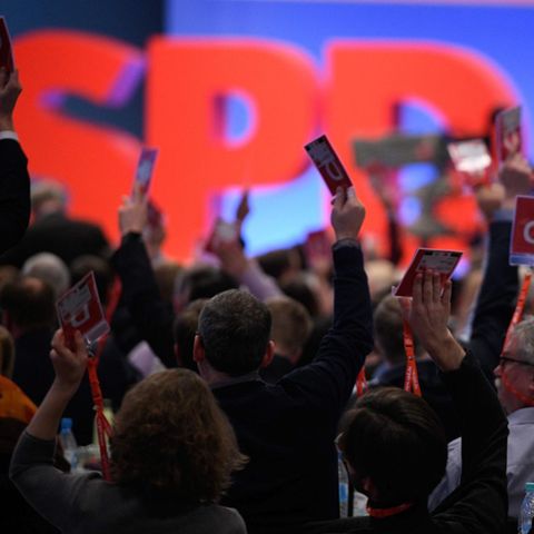 Vor einer blau beleuchteten Wand und großem "SPD" recken Delegierte auf dem Sonderparteitag ihre Abstimmungskarten hoch