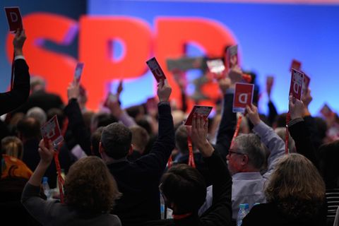Vor einer blau beleuchteten Wand und großem "SPD" recken Delegierte auf dem Sonderparteitag ihre Abstimmungskarten hoch