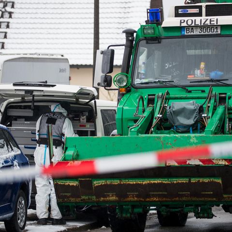 Vor dem Grundstück der Vermissten sucht ein Polizist in weißem Overall etwas in einem weißen VW-Bus, daneben ein grüner Unimog
