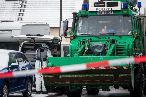 Vor dem Grundstück der Vermissten sucht ein Polizist in weißem Overall etwas in einem weißen VW-Bus, daneben ein grüner Unimog