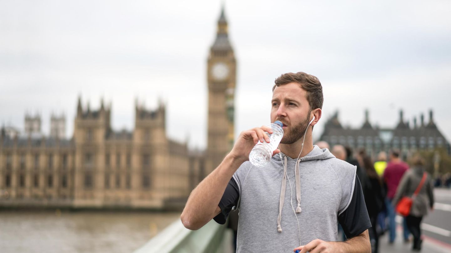 Ein Jogger steht vor dem Big Ben und trinkt aus einer Plastikflasche