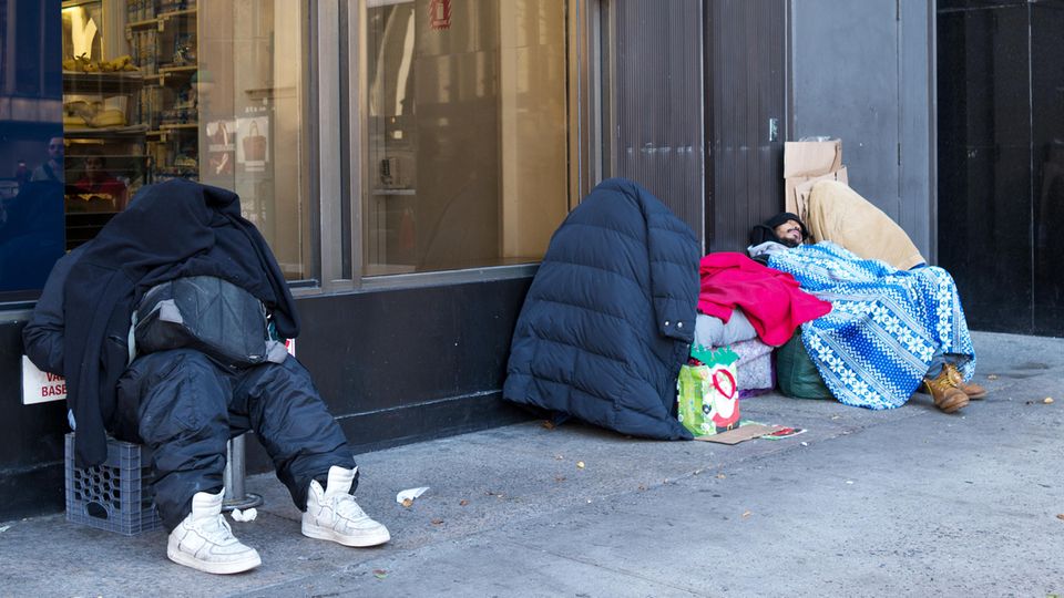 Obdachlose sitzen in vielen Schichten Kleidung auf dem Bürgersteig
