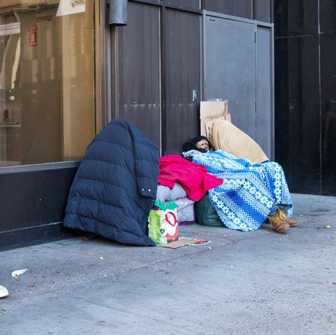 Obdachlose sitzen in vielen Schichten Kleidung auf dem Bürgersteig