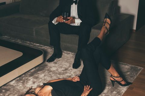 Ein älterer Herr sitzt im Anzug auf einer Couch, davor liegt eine junge Frau auf dem Rücken vor ihm (Symbolfoto)