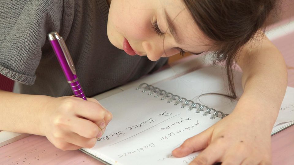 Schülerin Grundschule Rechtschreibung Eine Grundschülerin beugt sich über einen Block und schreibt mit einem Kugelschreiber einen Satz.
