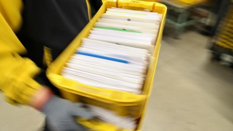 Ein Postbeamter trägt eine Kiste voller Briefe