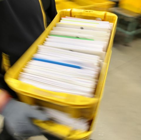 Ein Postbeamter trägt eine Kiste voller Briefe