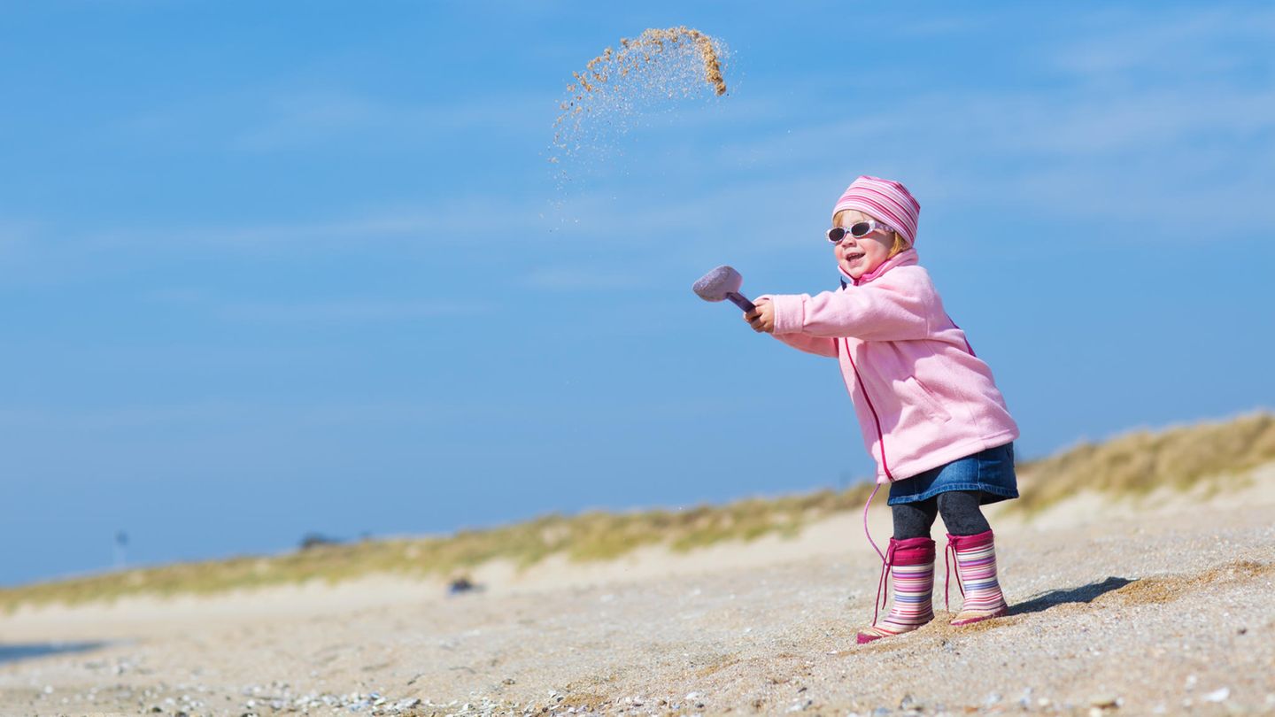Ein Mädchen in wetterfester Kleidung wirft eine Schaufel voll Sand in die Luft