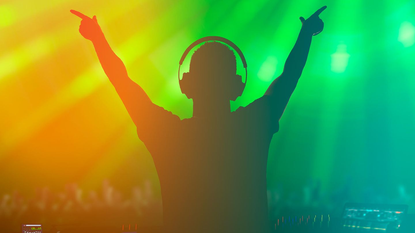 Ein DJ steht im Gegenlicht in einer Disco und reckt die Arme nach oben
