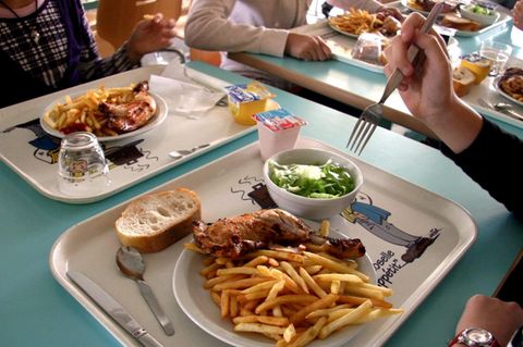 Auf einem Tablett ist ein Teller mit Pommes und einer Hähnchenkeule, eine Schale Salat und ein Stück Brot.