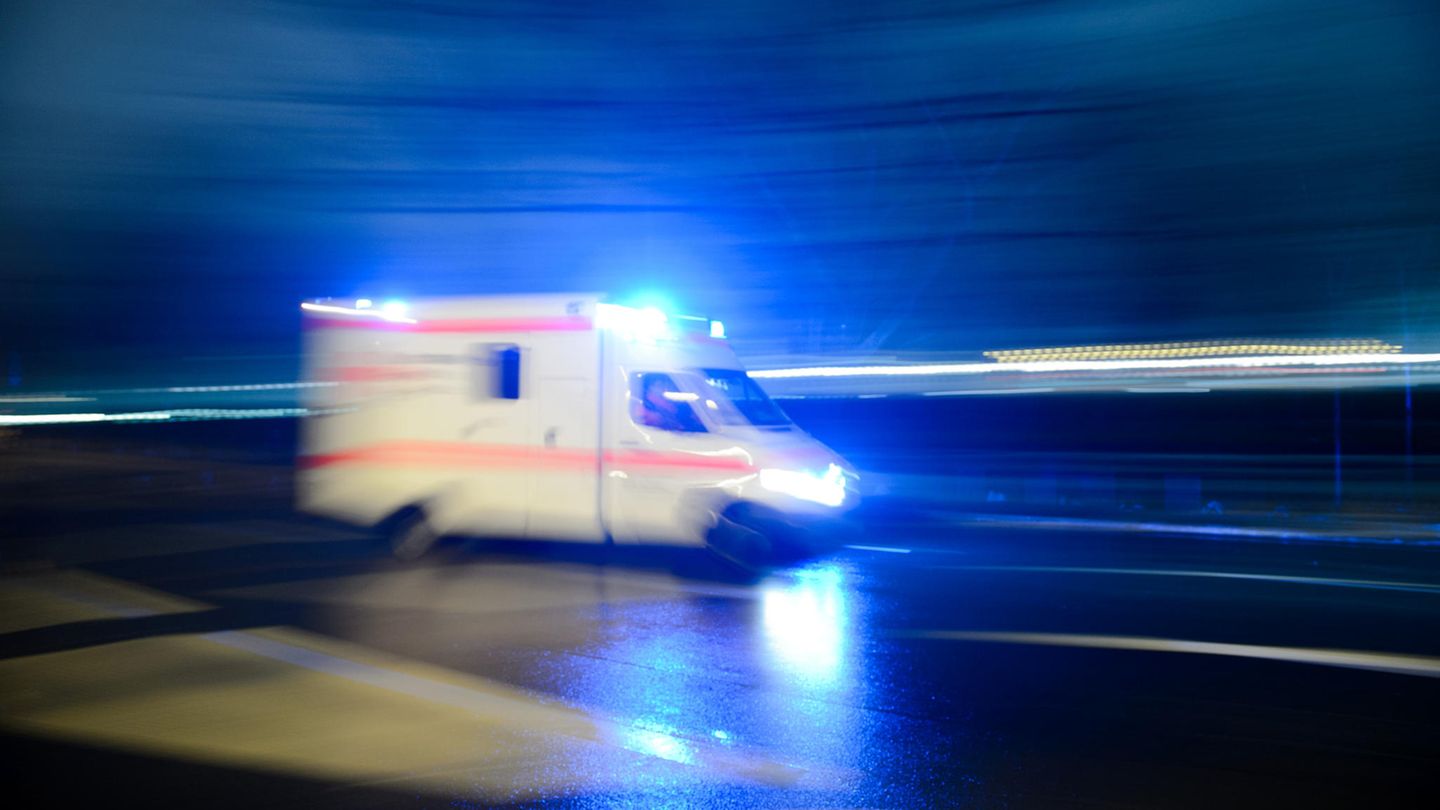 Ein Krankenwagen fährt mit Blaulicht durch eine dunkle, regennasse Straße in Berlin. Das Bild hat Bewegungsunschärfe