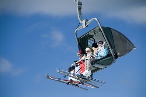 Vier Skifahrerinnen und Skifahrer sitzen in einem Vierer-Sessellift, am Himmel nur Schleierwölkchen