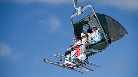 Vier Skifahrerinnen und Skifahrer sitzen in einem Vierer-Sessellift, am Himmel nur Schleierwölkchen
