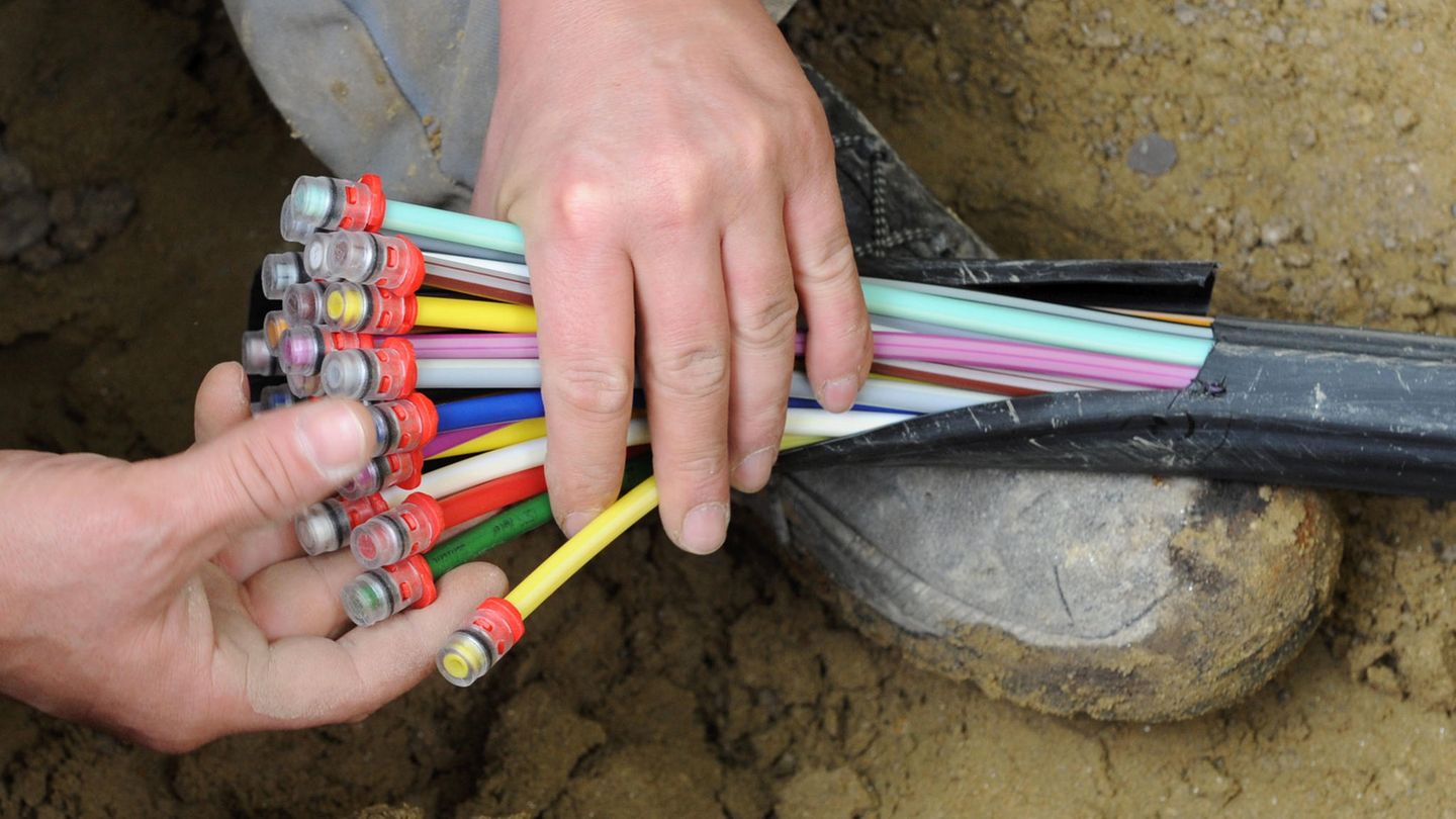 Ein Bauarbeiter kniet in einem Erdloch und hält in seinen Händen einen Strang mit unterschiedlich farbig markierten Kabeln