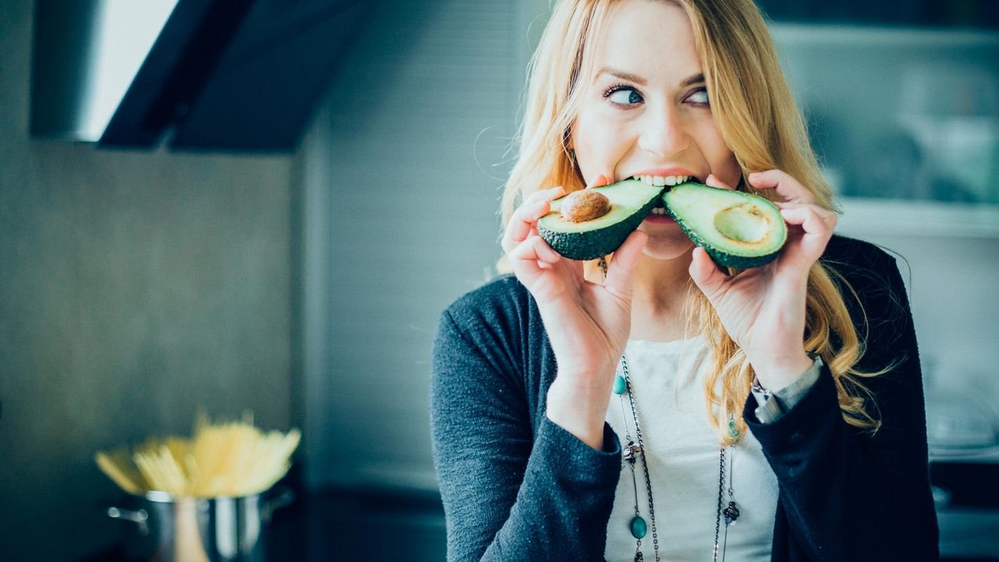 Eine junge Frau beißt in eine Avocado