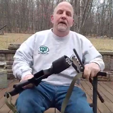 Ein älterer Mann mit Jeans und grauem Sweatshirt sitzt mit seiner zersägten AR-15 in den Händen auf einer Terrasse