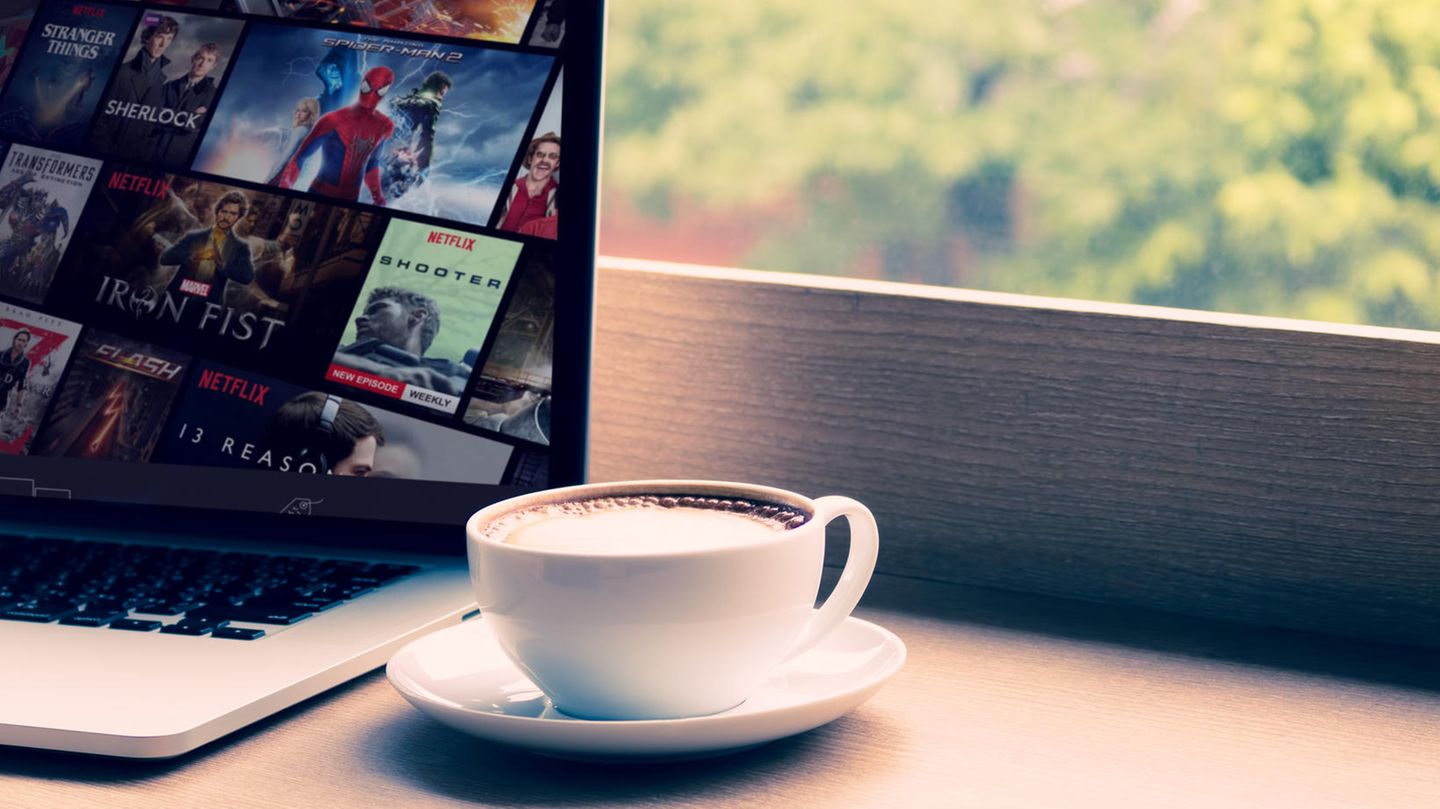 Eine Tasse Kaffee steht neben einem Laptop, auf dem das Streaming-Angebot von Netflix geöffnet ist.