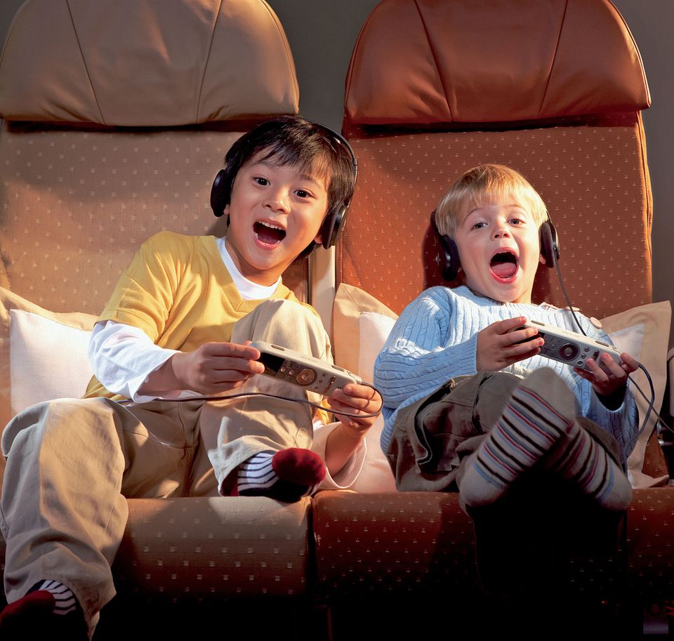Besser Reisen: Abgelenkt durch das Unterhaltungsprogramm an Bord: Kids mit der Fernbedienung in Händen. Abgelenkt durch das Unterhaltungsprogramm an Bord: Kids mit der Fernbedienung in Händen.