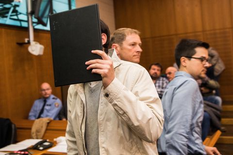 Angeklagter hält sich schwarze Mappe vor das Gesicht