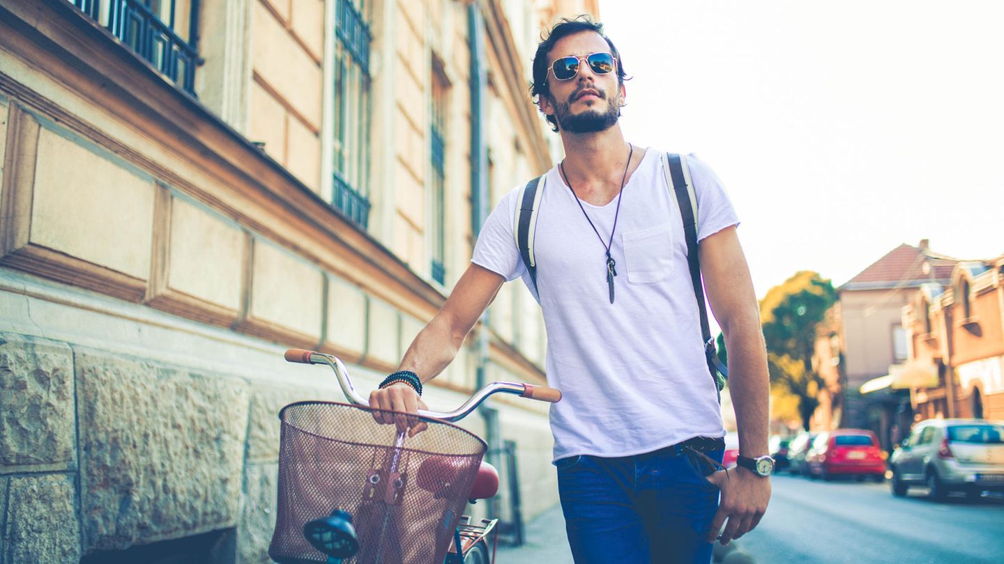 Junger Mann mit Sonnenbrille schiebt sein Fahrrad